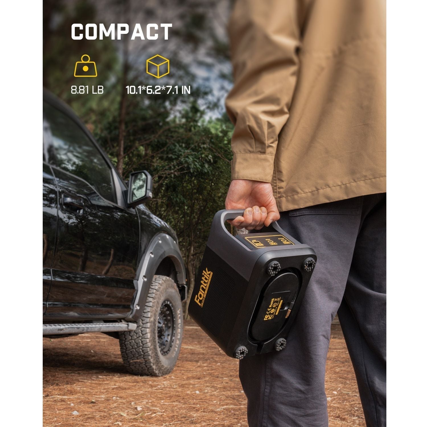Person holding a black Fanttik X9 Ultra portable tire inflator next to an off-road vehicle.